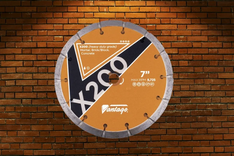 An orange Diamond Vantage X200 heavy-duty tuck point blades for mortar, brick, and concrete, hanging under a spotlight on a brick background.